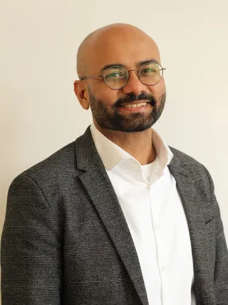 Indrajeet Patil, a man with round gold-framed glasses wearing a dark suit jacket and white shirt